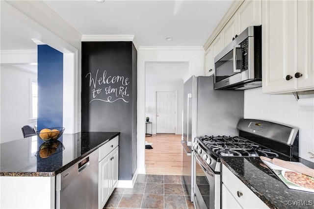 kitchen featuring tasteful backsplash, appliances with stainless steel finishes, ornamental molding, dark stone countertops, and white cabinetry