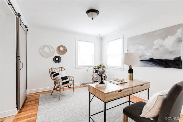 office featuring light wood-style floors, baseboards, and a barn door