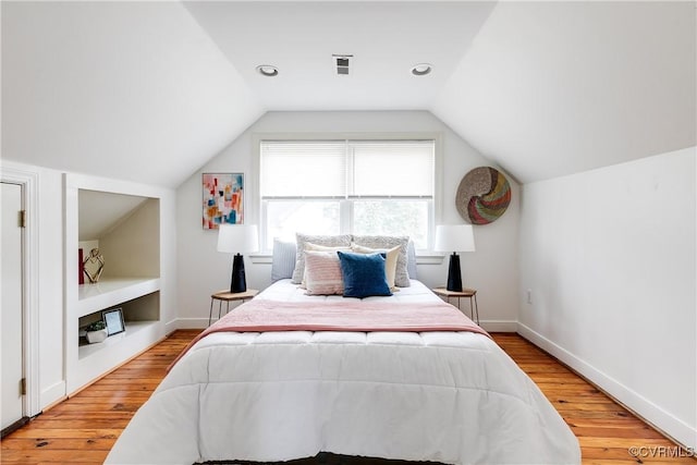 bedroom with vaulted ceiling, visible vents, light wood-style flooring, and baseboards