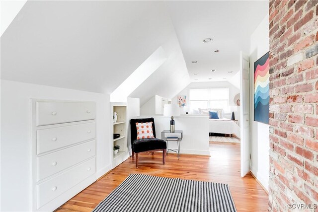 living area with vaulted ceiling, brick wall, light wood finished floors, and built in shelves