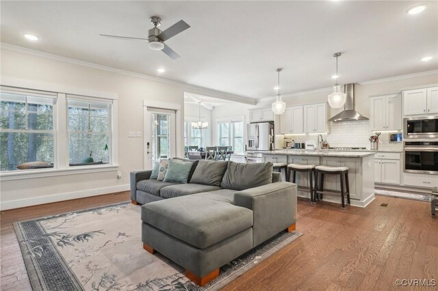 living room featuring recessed lighting, ornamental molding, wood finished floors, baseboards, and ceiling fan with notable chandelier