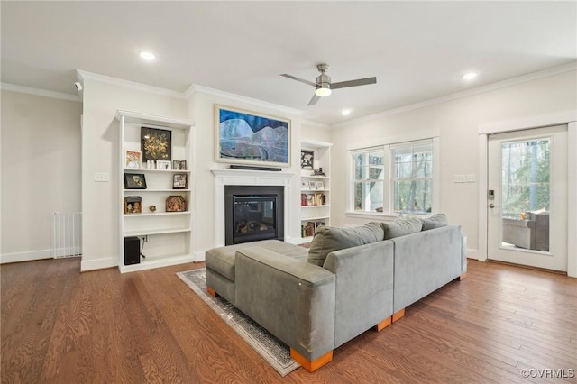 living area featuring a glass covered fireplace, crown molding, and wood finished floors