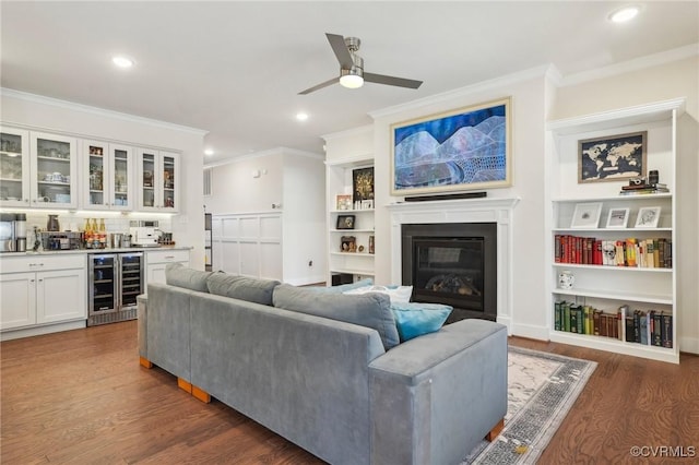 living area featuring beverage cooler, crown molding, wood finished floors, and a glass covered fireplace