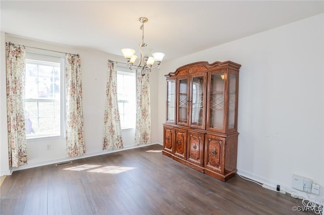 unfurnished dining area featuring visible vents, dark wood-style flooring, a wealth of natural light, and a notable chandelier