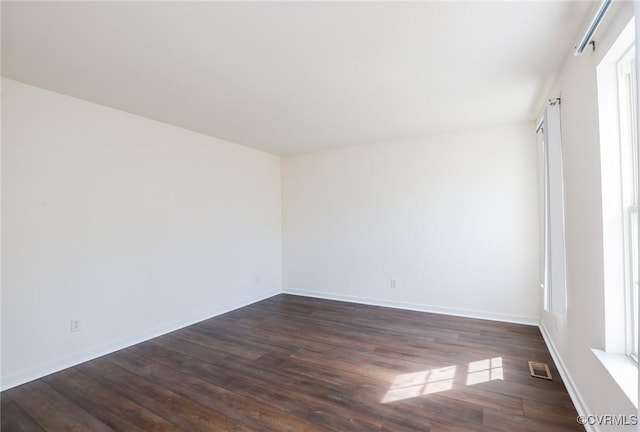 spare room featuring dark wood-style flooring, visible vents, and baseboards