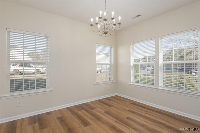 empty room featuring a chandelier, wood finished floors, visible vents, and baseboards