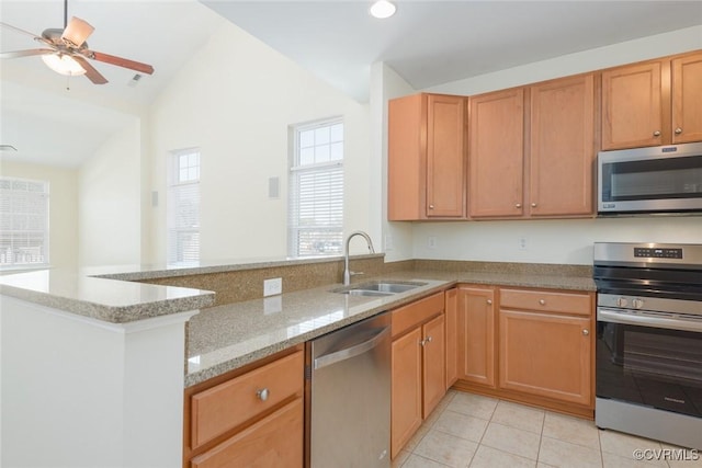 kitchen with light stone counters, lofted ceiling, appliances with stainless steel finishes, a sink, and a peninsula