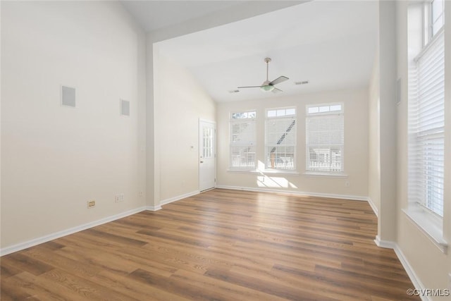 empty room featuring a wealth of natural light, baseboards, vaulted ceiling, and wood finished floors