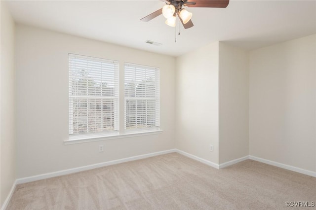 empty room with a ceiling fan, light colored carpet, visible vents, and baseboards