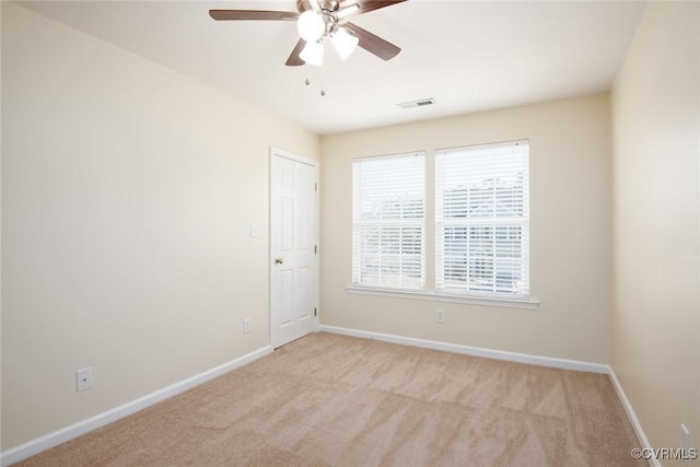 spare room with light carpet, a ceiling fan, visible vents, and baseboards