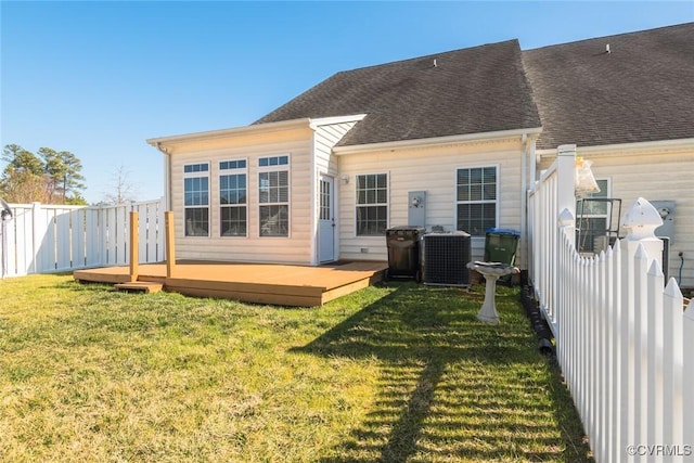 rear view of house featuring central AC unit, a shingled roof, fence, a lawn, and a wooden deck