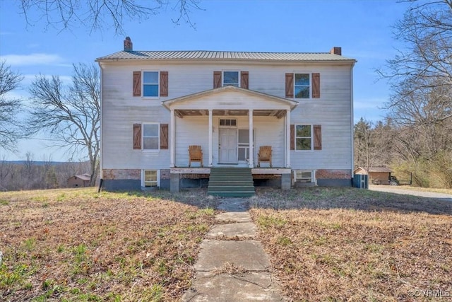 view of front facade featuring covered porch, metal roof, and a chimney