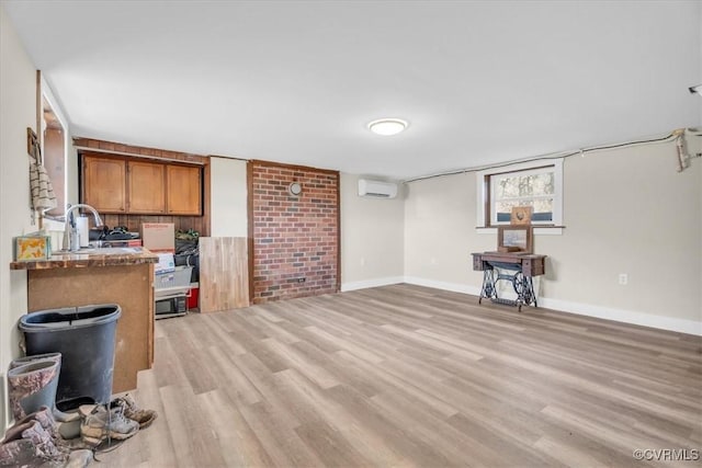 interior space featuring baseboards, brown cabinetry, a wall mounted air conditioner, light wood-type flooring, and a sink