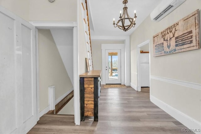 interior space with a wall unit AC, an inviting chandelier, baseboards, and wood finished floors