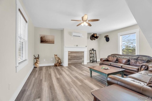 living area featuring baseboards, a ceiling fan, a wall mounted air conditioner, light wood-type flooring, and a fireplace