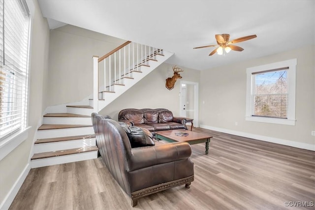 living area with a ceiling fan, wood finished floors, baseboards, and stairs