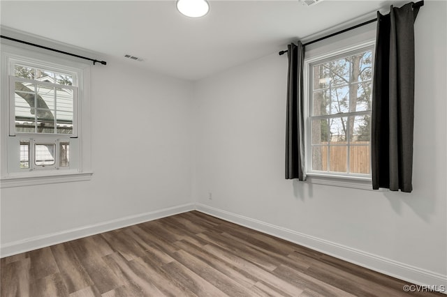 unfurnished room with baseboards, visible vents, and wood finished floors