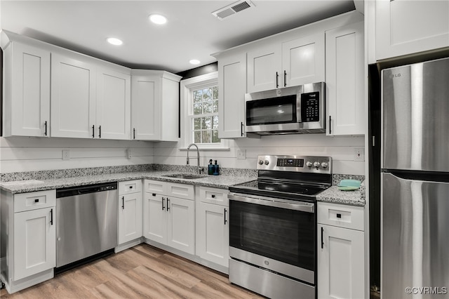 kitchen featuring visible vents, light wood-style flooring, appliances with stainless steel finishes, white cabinetry, and a sink