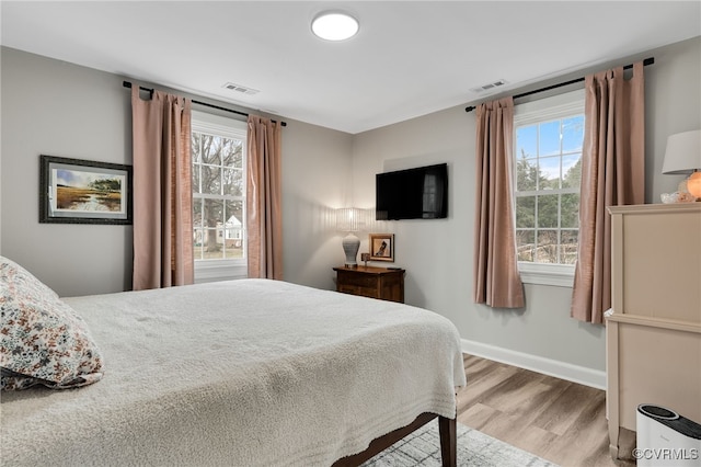 bedroom with multiple windows, visible vents, baseboards, and wood finished floors