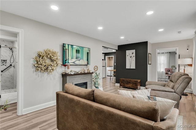 living room with light wood finished floors, recessed lighting, visible vents, a glass covered fireplace, and baseboards