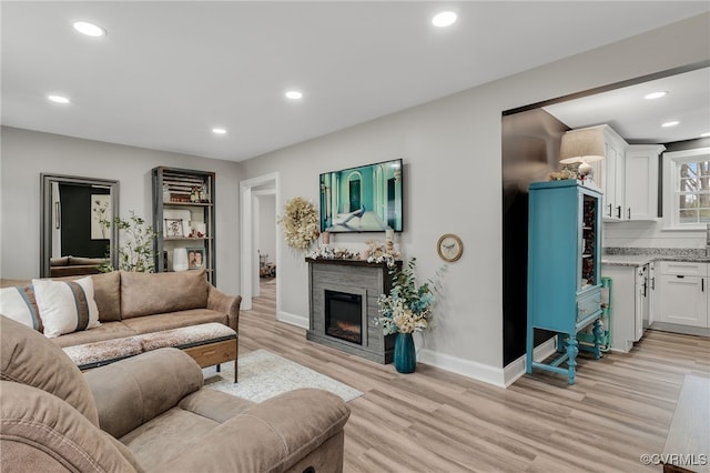 living room with recessed lighting, a glass covered fireplace, light wood-style flooring, and baseboards