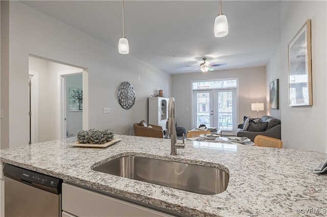 kitchen featuring dishwasher, light stone counters, open floor plan, hanging light fixtures, and a sink