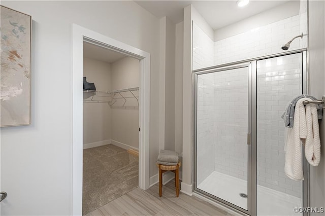 bathroom with a stall shower, a walk in closet, and baseboards