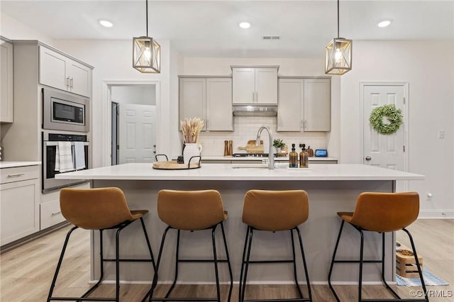 kitchen with tasteful backsplash, visible vents, appliances with stainless steel finishes, a breakfast bar area, and under cabinet range hood