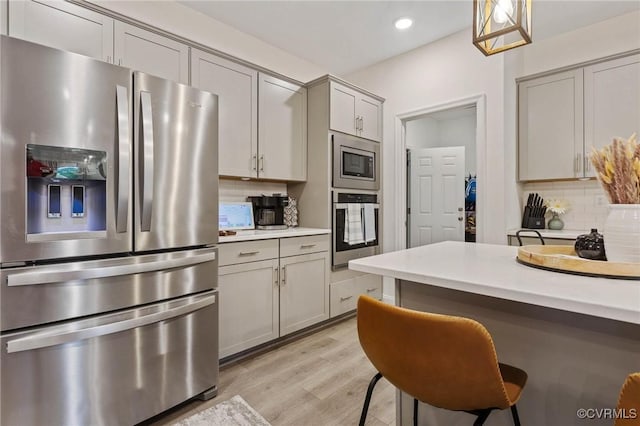 kitchen featuring stainless steel appliances, light countertops, decorative backsplash, gray cabinetry, and light wood-type flooring