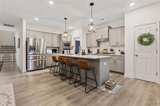 kitchen featuring stainless steel appliances, gray cabinets, under cabinet range hood, and a kitchen bar