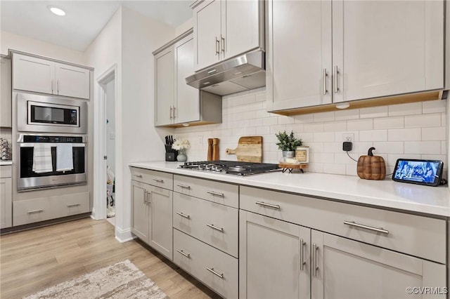 kitchen with light wood-style flooring, stainless steel appliances, light countertops, gray cabinetry, and under cabinet range hood