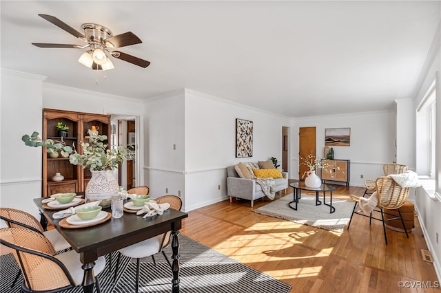 living area featuring ornamental molding, light wood-type flooring, baseboards, and a ceiling fan