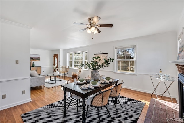 dining space featuring baseboards, a fireplace, a ceiling fan, and wood finished floors