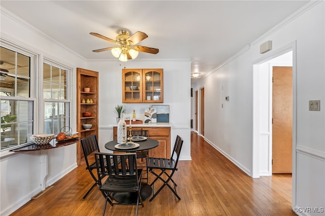 dining room featuring a ceiling fan, wood-type flooring, crown molding, and baseboards