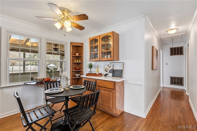 dining area featuring crown molding, wood finished floors, visible vents, and attic access