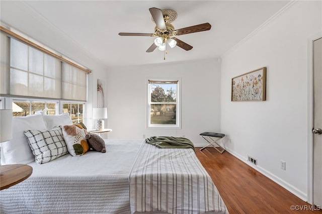 bedroom with baseboards, visible vents, a ceiling fan, ornamental molding, and wood finished floors