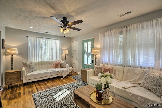 living room with a textured ceiling, wood finished floors, visible vents, and a ceiling fan