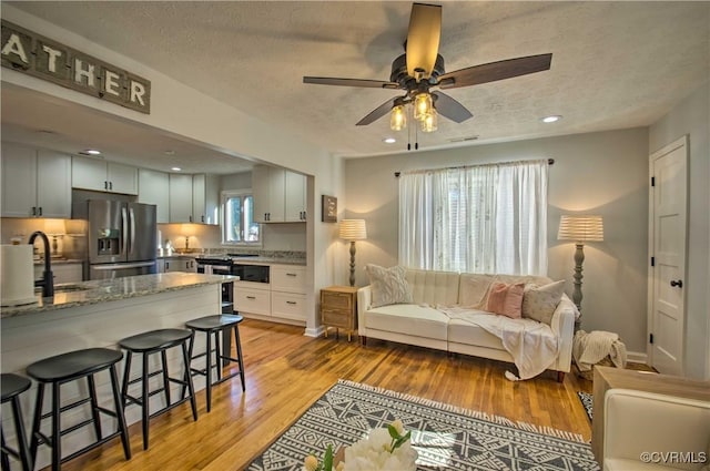 living area with a ceiling fan, light wood-type flooring, a textured ceiling, and recessed lighting