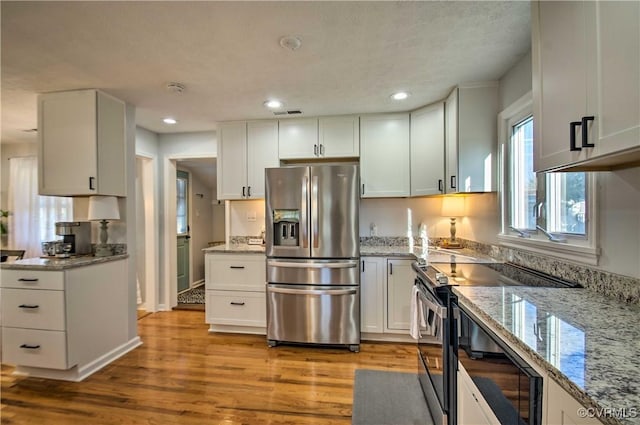 kitchen with stainless steel appliances, light wood-type flooring, white cabinetry, and light stone counters