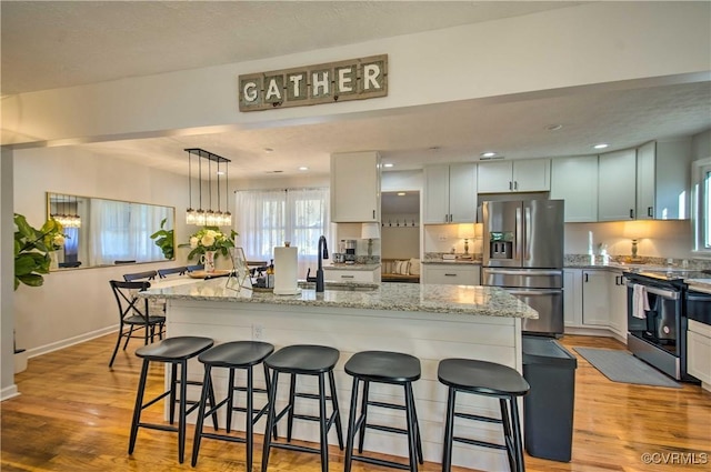 kitchen featuring light wood finished floors, baseboards, appliances with stainless steel finishes, a kitchen bar, and a sink