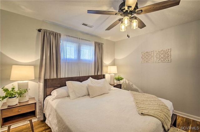 bedroom featuring a ceiling fan, visible vents, baseboards, and wood finished floors