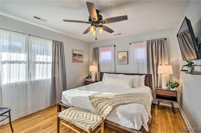 bedroom with a ceiling fan, light wood-type flooring, visible vents, and baseboards