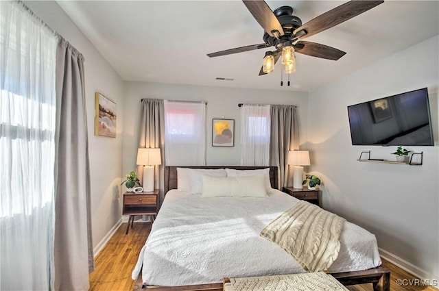 bedroom with ceiling fan, light wood finished floors, visible vents, and baseboards