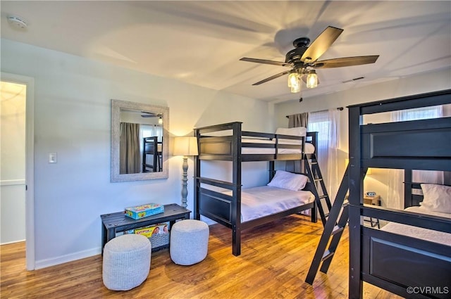 bedroom with ceiling fan, wood finished floors, visible vents, and baseboards