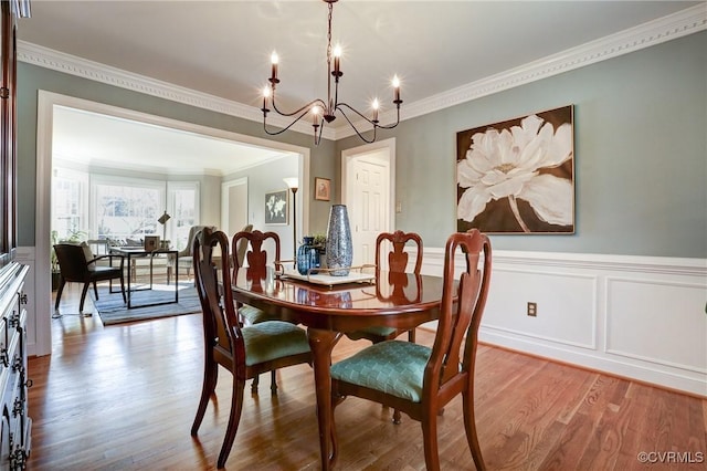 dining space with ornamental molding, a wainscoted wall, a notable chandelier, and wood finished floors