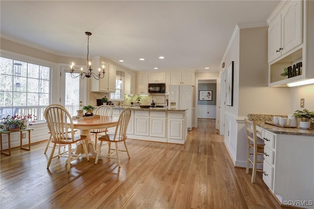 dining room featuring recessed lighting, a wainscoted wall, ornamental molding, light wood-type flooring, and an inviting chandelier