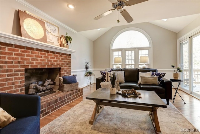 living room with vaulted ceiling with skylight, a brick fireplace, wood finished floors, and crown molding