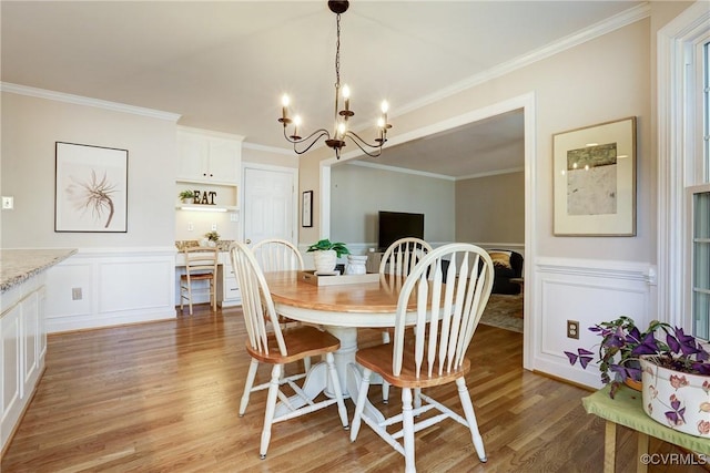 dining room with light wood-style floors, ornamental molding, a notable chandelier, and a wainscoted wall