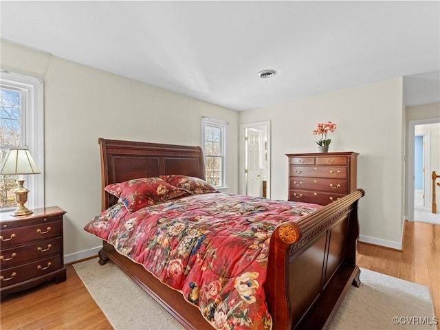 bedroom featuring baseboards, multiple windows, visible vents, and wood finished floors