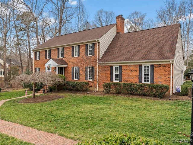 colonial inspired home with a front yard, a shingled roof, a chimney, and brick siding